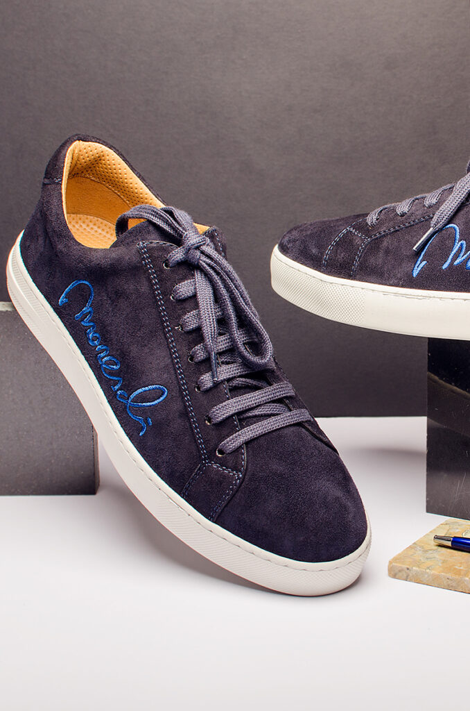 Still-life photography – sneakers di lusso Moreschi in camoscio blu con dettagli in blu elettrico, esposte su piedistallo di marmo.