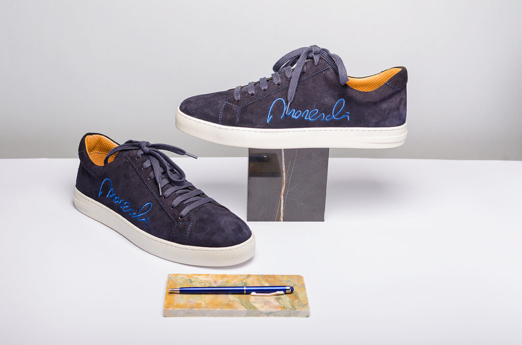 Still-life photography – sneakers di lusso Moreschi Signature Edition in camoscio blu con dettagli elettrici, esposte su piedistallo in marmo.