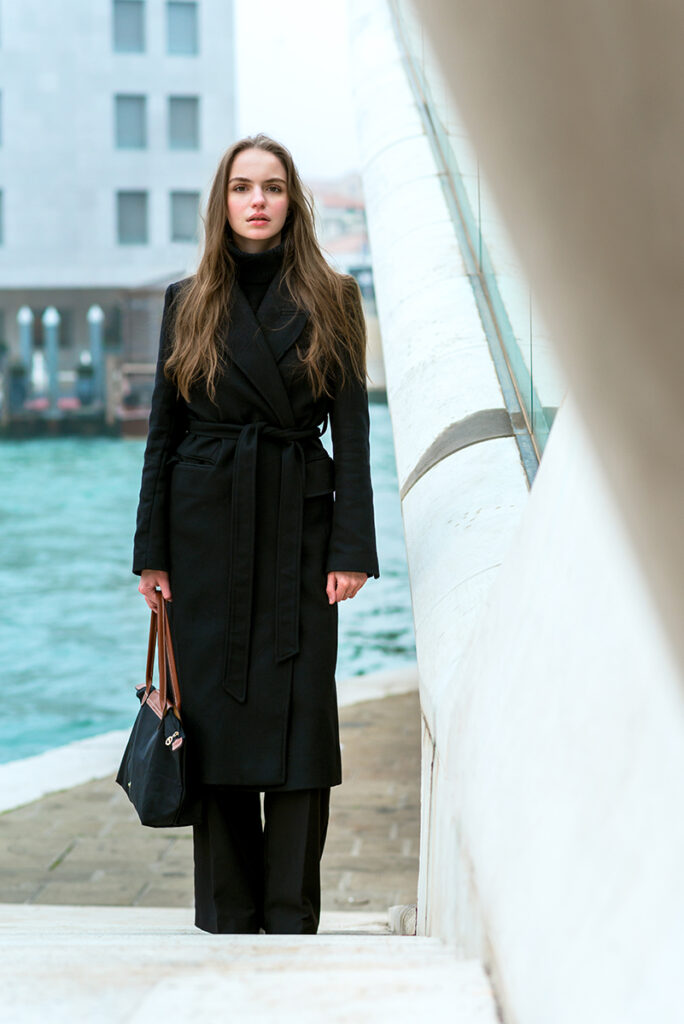 Modella in cappotto nero lungo presso un ambiente urbano di Venezia, scatto di Marius Cruceriu.