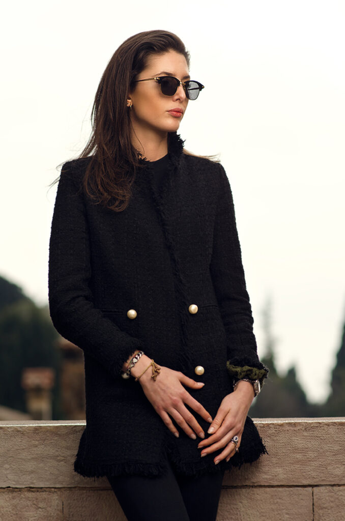 Modella con occhiali da sole artigianali indossa cappotto nero elegante, campagna eyewear Lucy of Syracuse fotografata da Marius Cruceriu