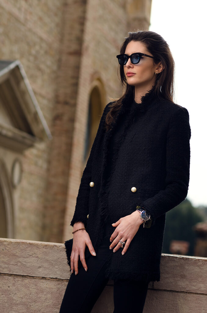 Modella con occhiali da sole artigianali e cappotto nero, fotografia moda per il brand Lucy of Syracuse in ambientazione italiana