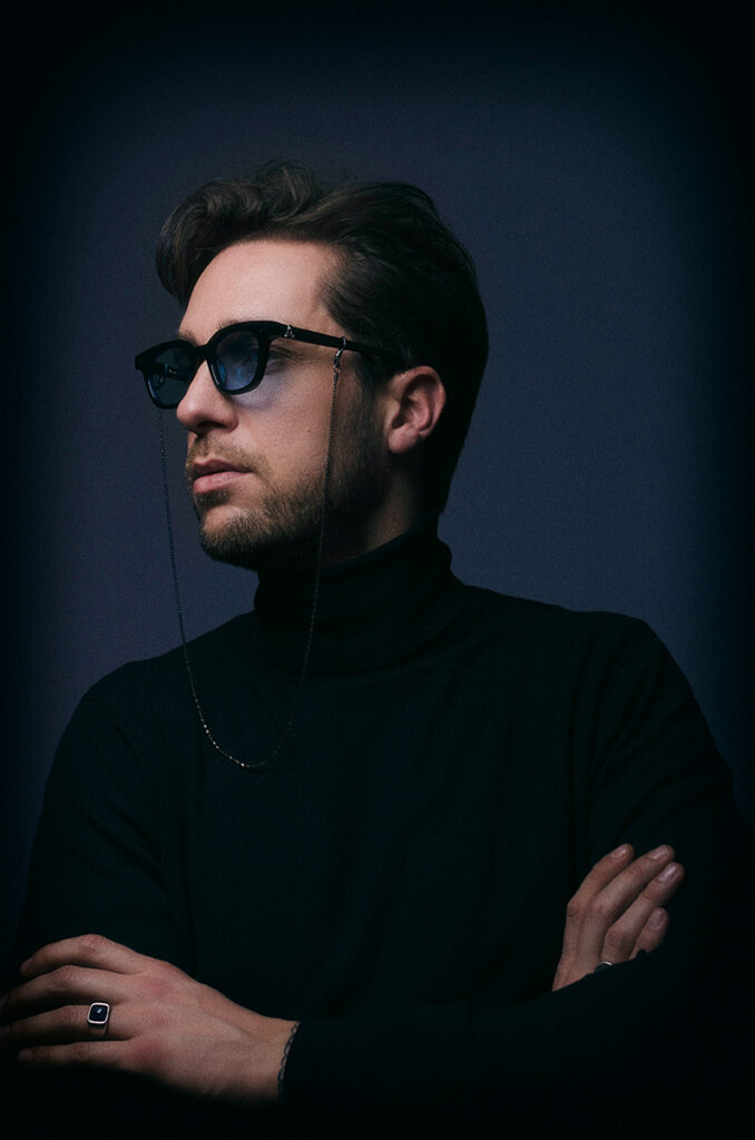 Ritratto maschile con occhiali scuri e catena eyewear in studio, fotografia moda elegante e contemporanea