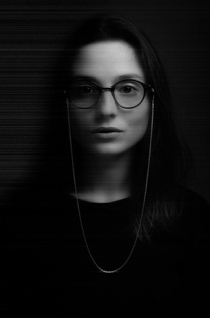 Donna con occhiali rotondi e catena in ritratto artistico bianco e nero con effetto movimento leggero