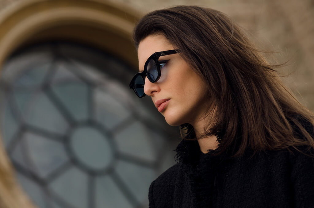 Profilo femminile con occhiali da sole neri, fotografia ambientata in location storica italiana per collezione eyewear