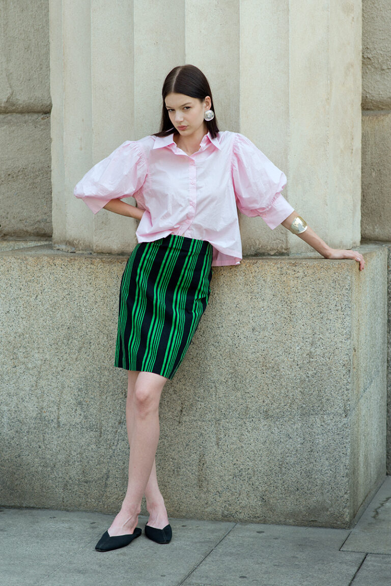 Modella Zuzanna in posa rilassata durante un test per Supreme Management Milano, appoggiata a una parete di pietra con camicia rosa a maniche voluminose e gonna a righe verdi, fotografata da Marius Cruceriu.