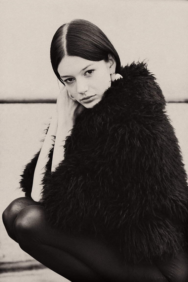 Modella Zuzanna durante un test per Supreme Management Milano, in posa accovacciata con cappotto nero in pelliccia e collant aderenti, fotografata da Marius Cruceriu.