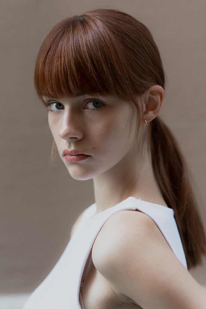 Primo piano di profilo della modella Agata durante un test per Tank Agency a Milano, con capelli ramati raccolti in coda bassa e top bianco, fotografata da Marius Cruceriu.