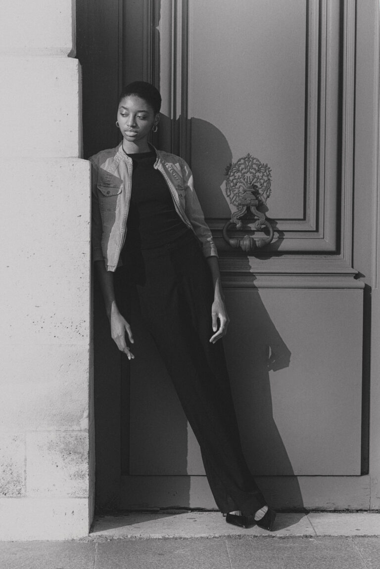 Modella Annaya a Parigi in bianco e nero, posa appoggiata a un portone con giacca di jeans e pantaloni scuri, scatto urban chic per test agenzia The Face, fotografata da Marius Cruceriu.