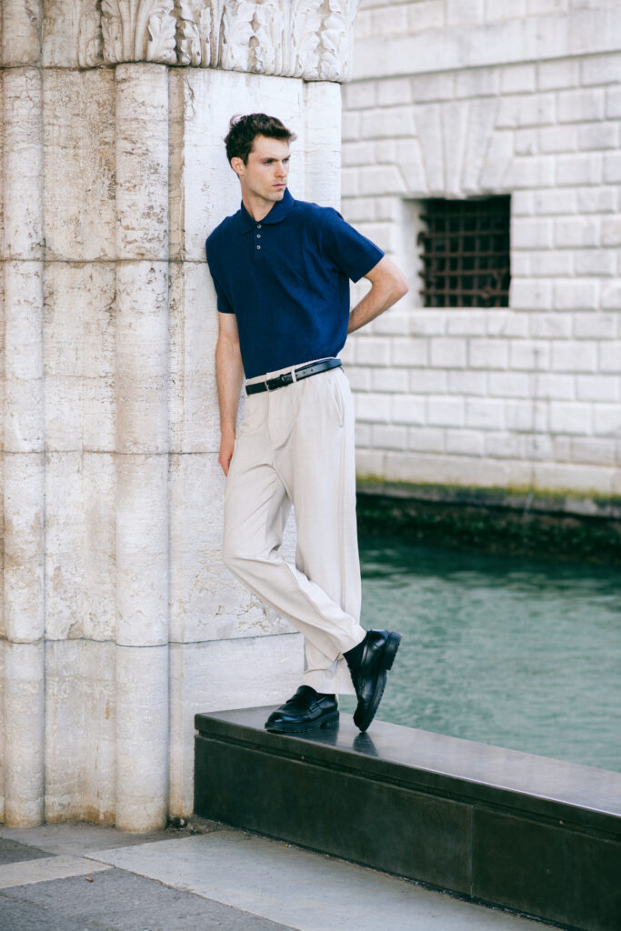 Modello Blake a Venezia in posa a figura intera appoggiato a una colonna, con polo blu e pantaloni chiari, scatto di moda maschile a colori realizzato da Marius Cruceriu.