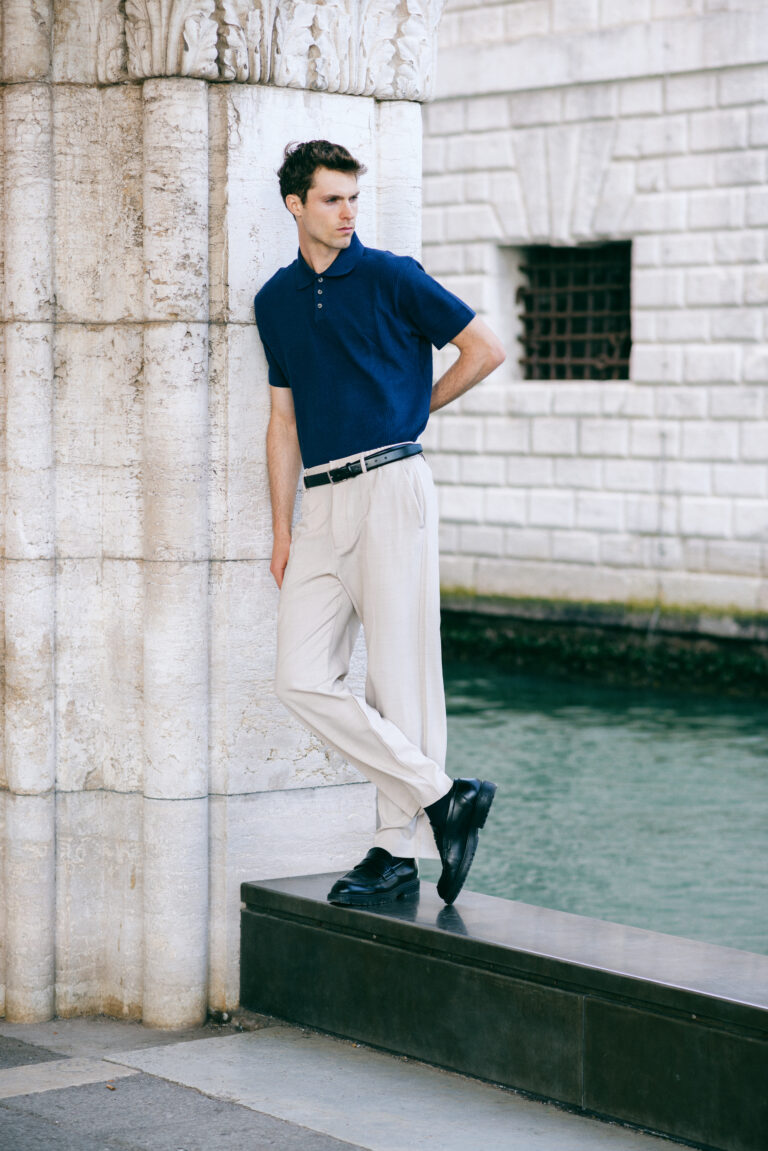 Modello Blake a Venezia in posa a figura intera appoggiato a una colonna, con polo blu e pantaloni chiari, scatto di moda maschile a colori realizzato da Marius Cruceriu.