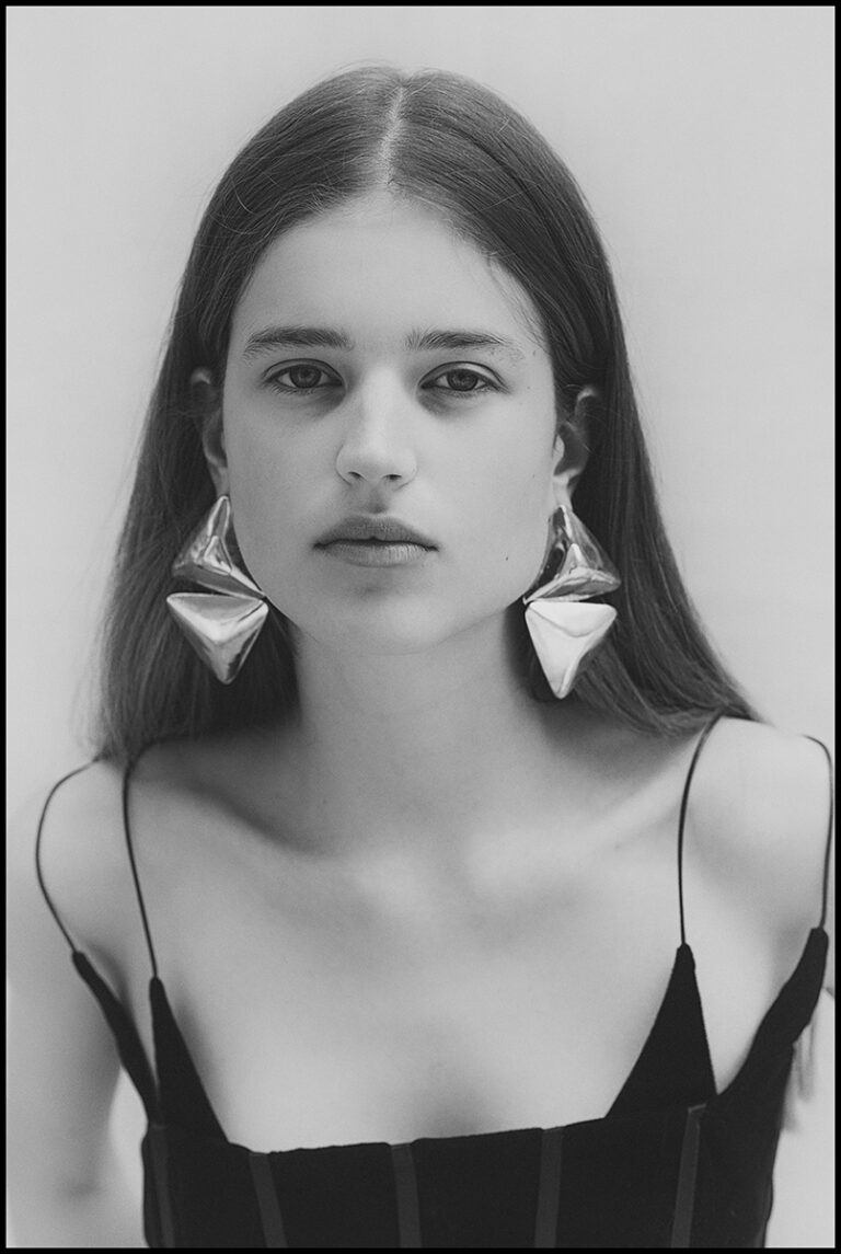 Ritratto in bianco e nero della modella Juta durante un test per Supreme Management Milano, con top nero a spalline sottili e maxi orecchini scultorei metallici, fotografata da Marius Cruceriu.