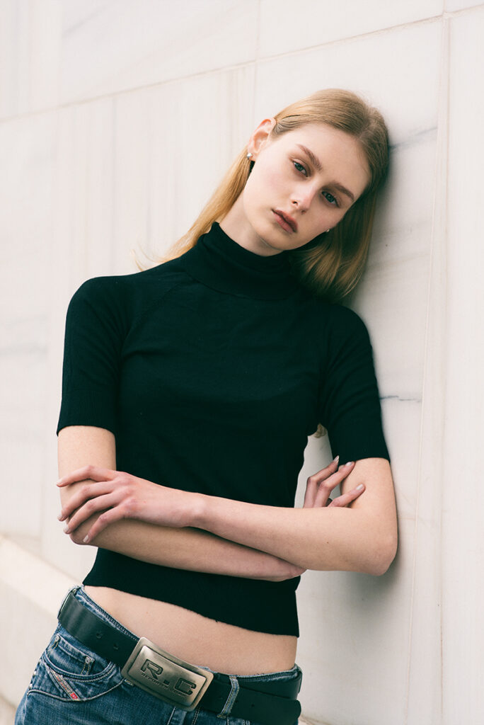 Modella Kornelia a Milano, posa rilassata appoggiata al muro con dolcevita nero e jeans Diesel, test model per agenzia Fabbrica Milano, scatto di Marius Cruceriu.