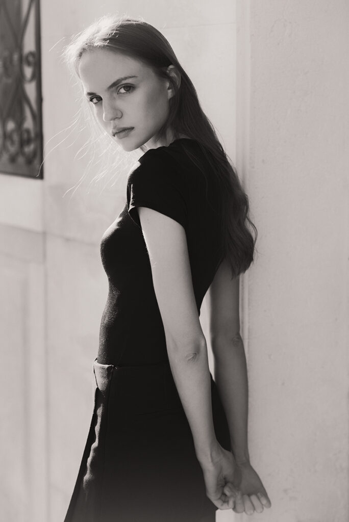 Modella Lidyia per Novastars Models a Venezia, ritratta di tre quarti in bianco e nero con maglia nera attillata a maniche corte, pantaloni neri e sguardo in camera, fotografata da Marius Cruceriu.​