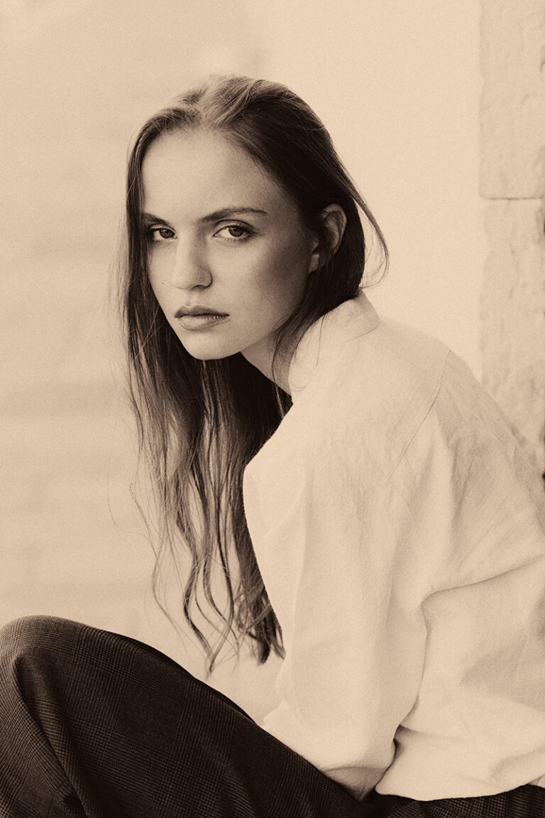 Modella Lidyia per Novastars Models a Venezia, ritratta di profilo in bianco e nero mentre è seduta, con camicia bianca e pantaloni a quadri, fotografata da Marius Cruceriu.