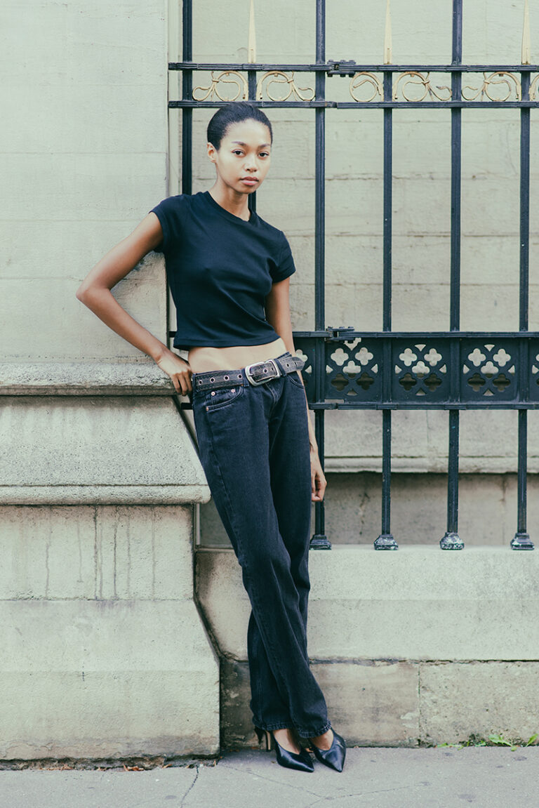 Modella Zoe a Parigi per The Face Paris, scatto street style a colori a figura intera appoggiata a una cancellata, look minimal con t-shirt nera e jeans scuri, test model realizzato da Marius Cruceriu.