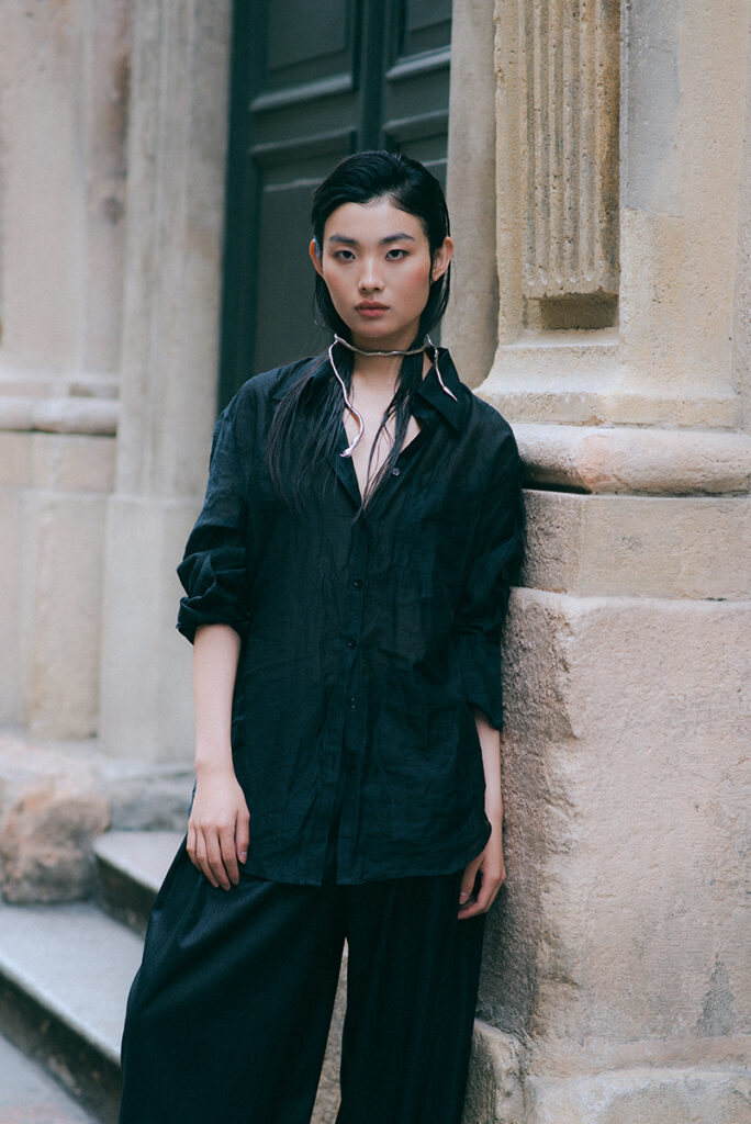 Dettaglio editorials a colori della modella Liu per "Of Shadows and Silk" su L'Officiel Baltic. Indossa una camicia nera trasparente di Mine de Rien Couture e un gioiello scultura al collo. Fotografia di Marius Cruceriu.