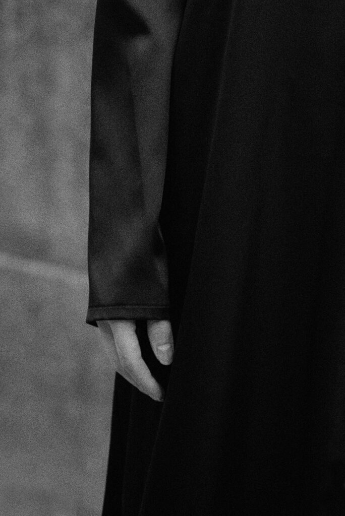 Dettaglio astratto in bianco e nero: mano della modella Liu lungo il fianco su seta nera scura. Editoriale "Of Shadows and Silk" per L'Officiel Baltic. Fotografia minimalista di Marius Cruceriu.